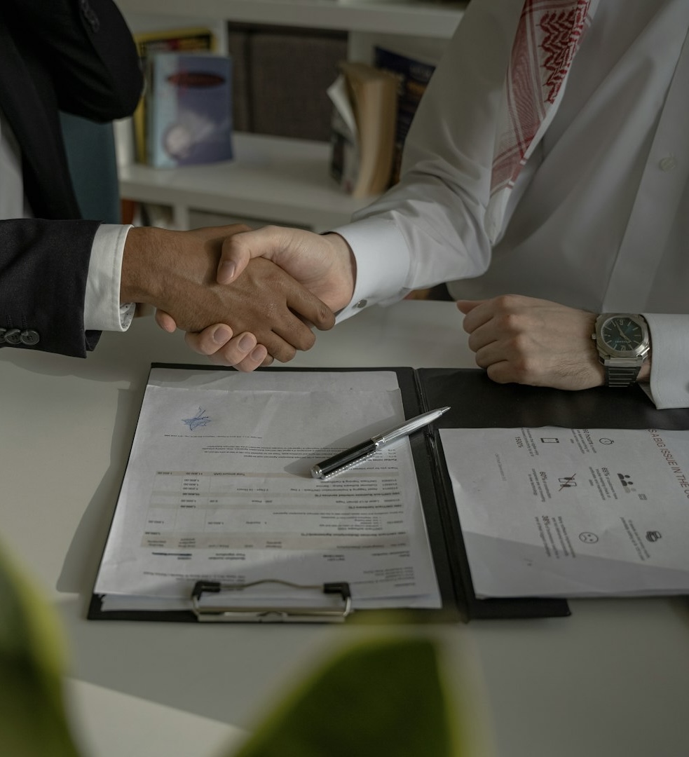 Two professionals shaking hands over signed documents on a desk, symbolizing agreement, trust, and a finalized contract.