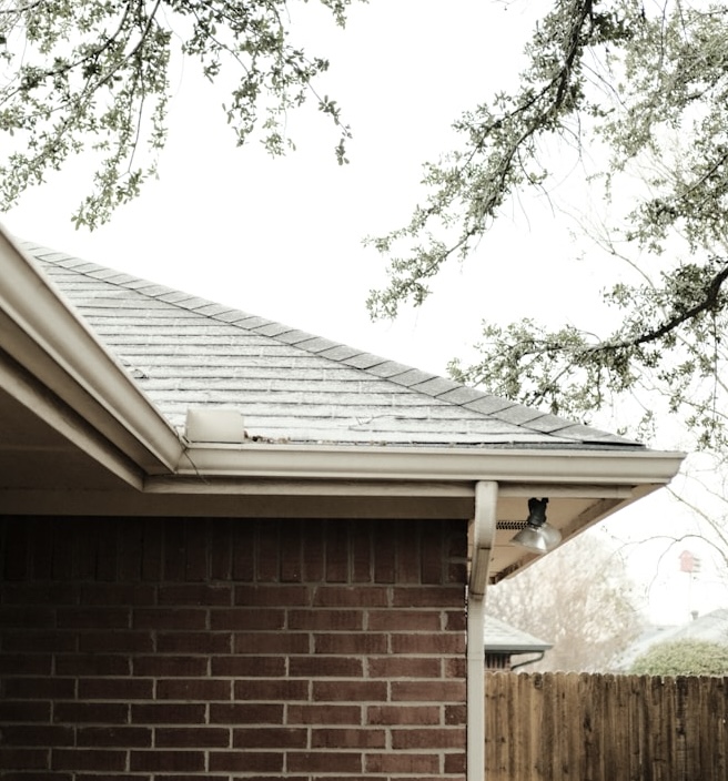 Exterior view of a house with a sloped roof, gutter system, and brick wall, highlighting general building maintenance.