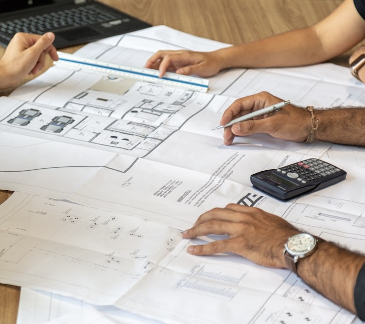 Two people reviewing construction plans on a table, measuring and discussing a building project