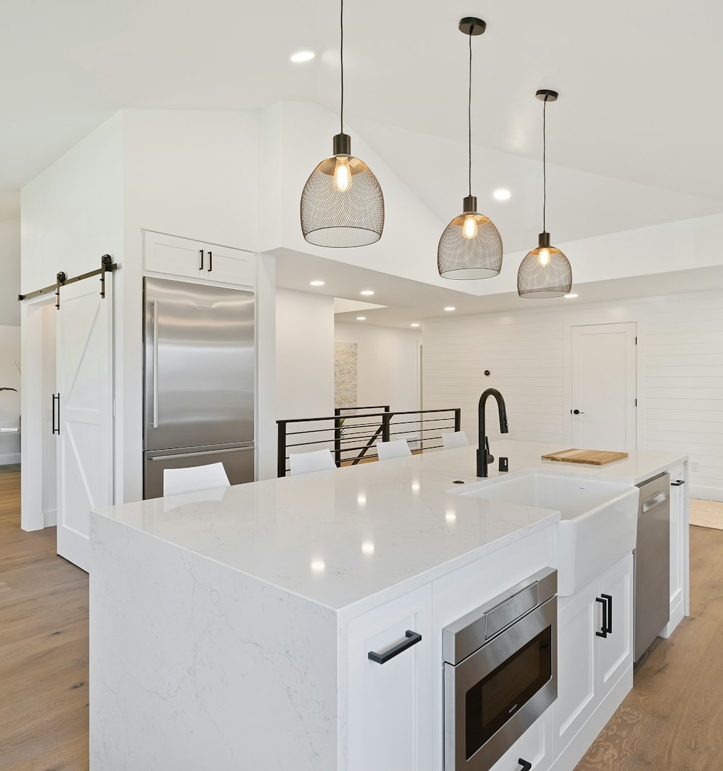 A modern, newly renovated kitchen with a white island, stainless steel appliances, and hanging pendant lights.